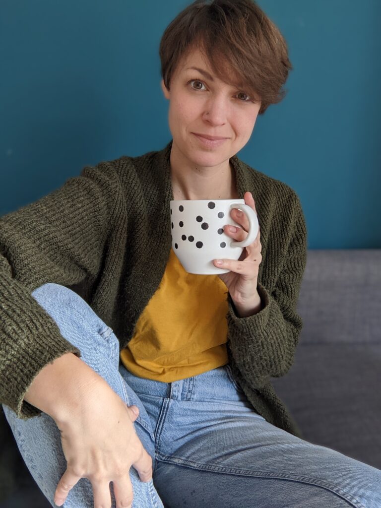 Lisa sitzt mit einer Tasse in der Hand auf dem Sofa.